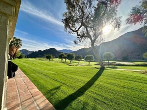 A well-maintained grassy area with trees and mountains in the background.