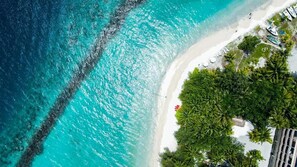 Vista aérea de una playa con aguas turquesas cristalinas, arena blanca y exuberante vegetación verde.