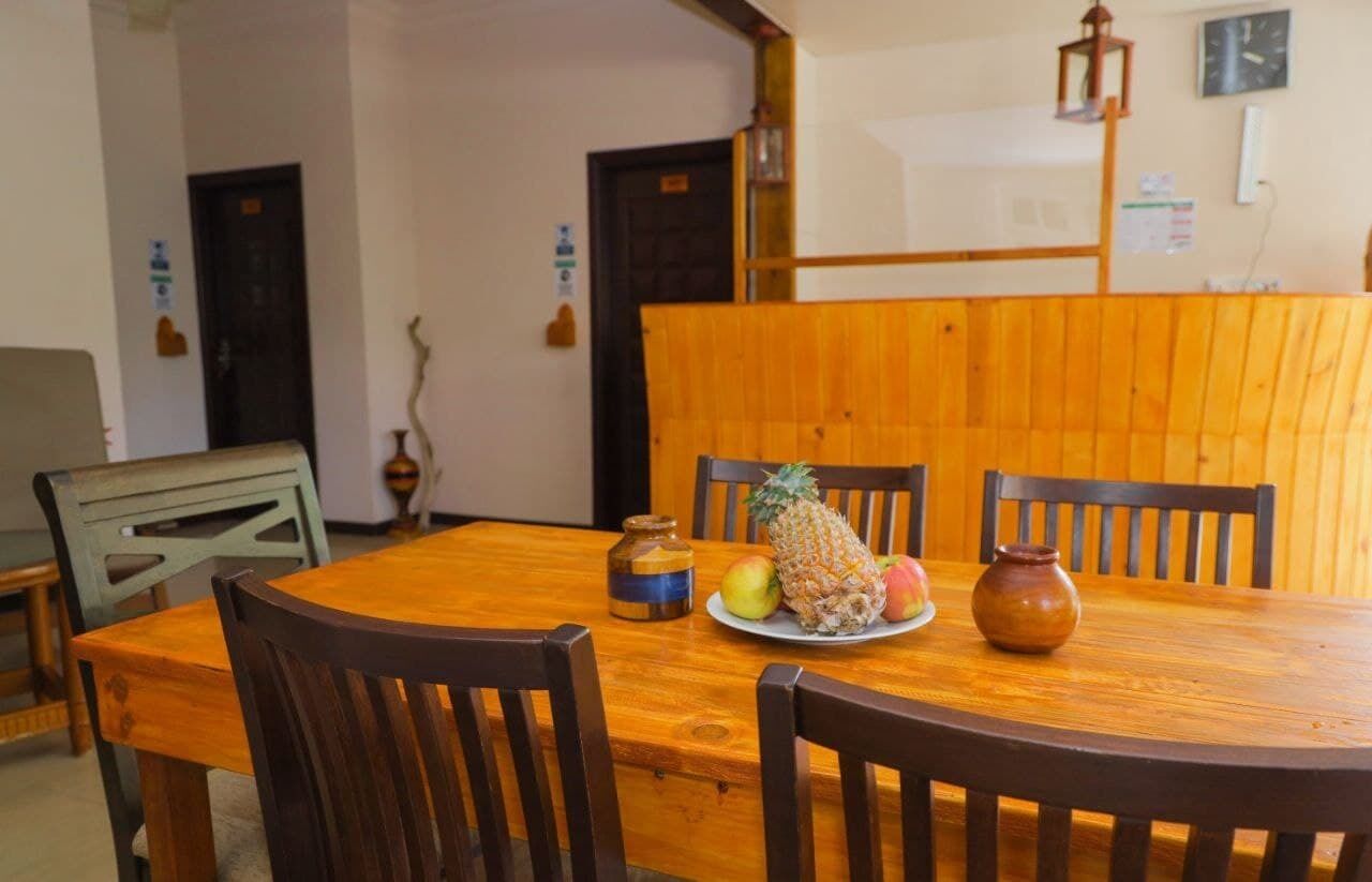 A wooden dining table with chairs, a pineapple, apples, and a vase.