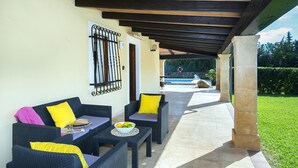 An outdoor patio with wicker furniture, a table with a bowl of fruit, and a view of a swimming pool. - Bacana, Finca 5StarsHome Mallorca (Puerto Pollensa)