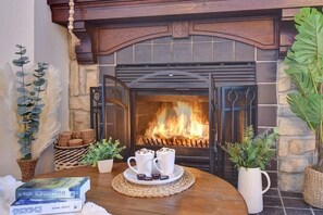A fireplace with a fire, surrounded by decorative plants and a table with books and a tray of hot beverages. - Tremblant village SKI resort, 10 m walk or shuttle (Mont-Tremblant)