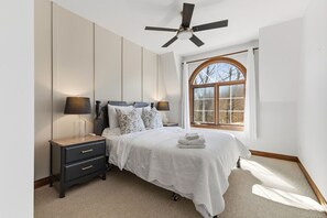 A bedroom with a bed, bedside lamps, a nightstand, a ceiling fan, and a window with curtains. - Tremblant village SKI resort, 10 m walk or shuttle (Mont-Tremblant)