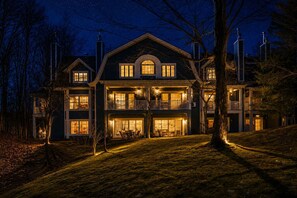 A large, multi-story house with a prominent central entrance, multiple balconies, and a well-lit facade. - Tremblant village SKI resort, 10 m walk or shuttle (Mont-Tremblant)