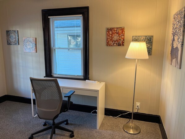 Une pièce comprenant un bureau blanc, un fauteuil de bureau noir, un lampadaire et des œuvres d’art décoratives accrochées au mur.