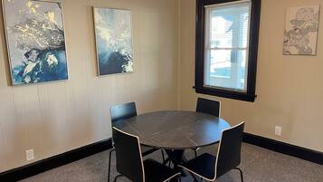 A conference room with a round table, four chairs, and three framed artworks on the walls.