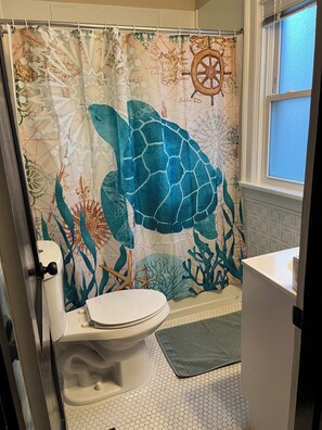 Une salle de bain avec un rideau de douche orné d’un motif de tortue de mer, des toilettes et un lavabo.