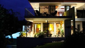 A two-story house with a balcony, outdoor seating, and potted plants. - Moonshine Inn — Pool Level Suite , Moonshine Inn -- Pool-Level 2BR Suite (Quepos)