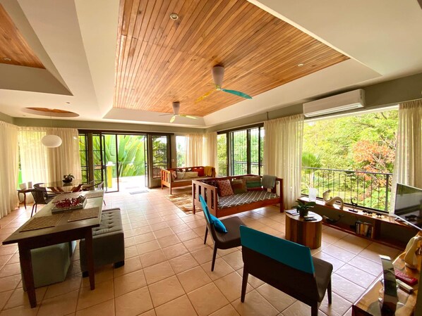 A spacious living area with a wooden ceiling, a dining table, a sofa, and a TV. - Moonshine Inn - 1 BR Studio Loft with Ocean & Jungle Views, Moonshine Inn -- 1BR Studio Loft (Quepos)