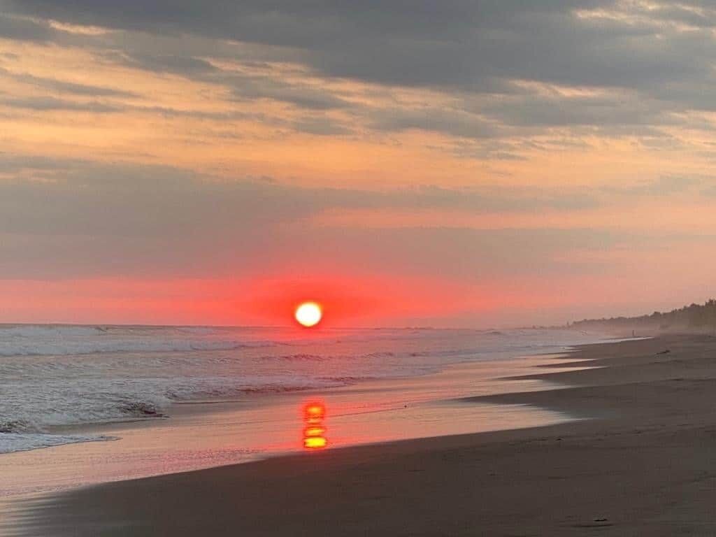 Escena de playa con un atardecer sobre el océano.