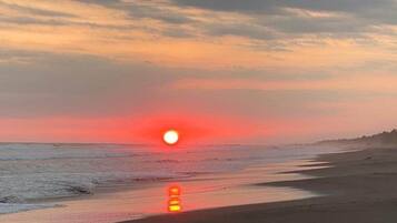 Escena de playa con un atardecer sobre el océano.