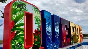 A colorful outdoor sign with the word "OCEAN" in large letters, surrounded by tropical leaf and flower illustrations. - Moonshine Inn - 1 BR Studio Loft with Ocean & Jungle Views, Moonshine Inn -- 1BR Studio Loft (Quepos)