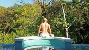 Un homme est assis au bord d’une piscine, avec un arbre en arrière-plan.