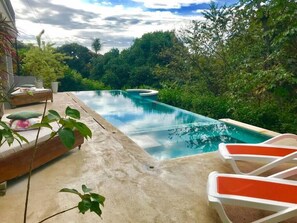 An infinity pool with a wooden deck and lounge chairs, surrounded by lush greenery. - Moonshine Inn - 1 BR Studio Loft with Ocean & Jungle Views, Moonshine Inn -- 1BR Studio Loft (Quepos)