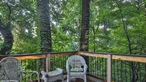 A wooden deck with wicker chairs and a table, surrounded by trees.