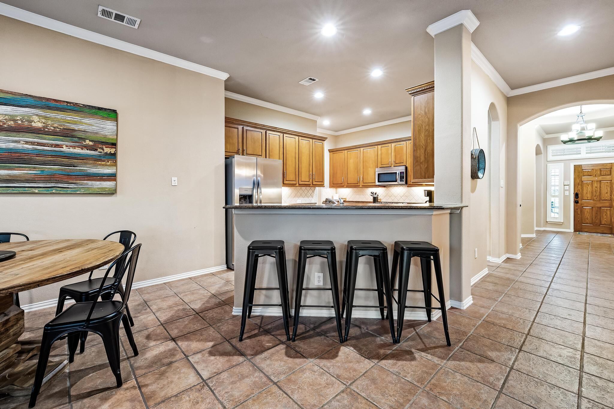 A modern kitchen with wooden cabinets, a central island with stools, and a dining area with a round table and chairs.