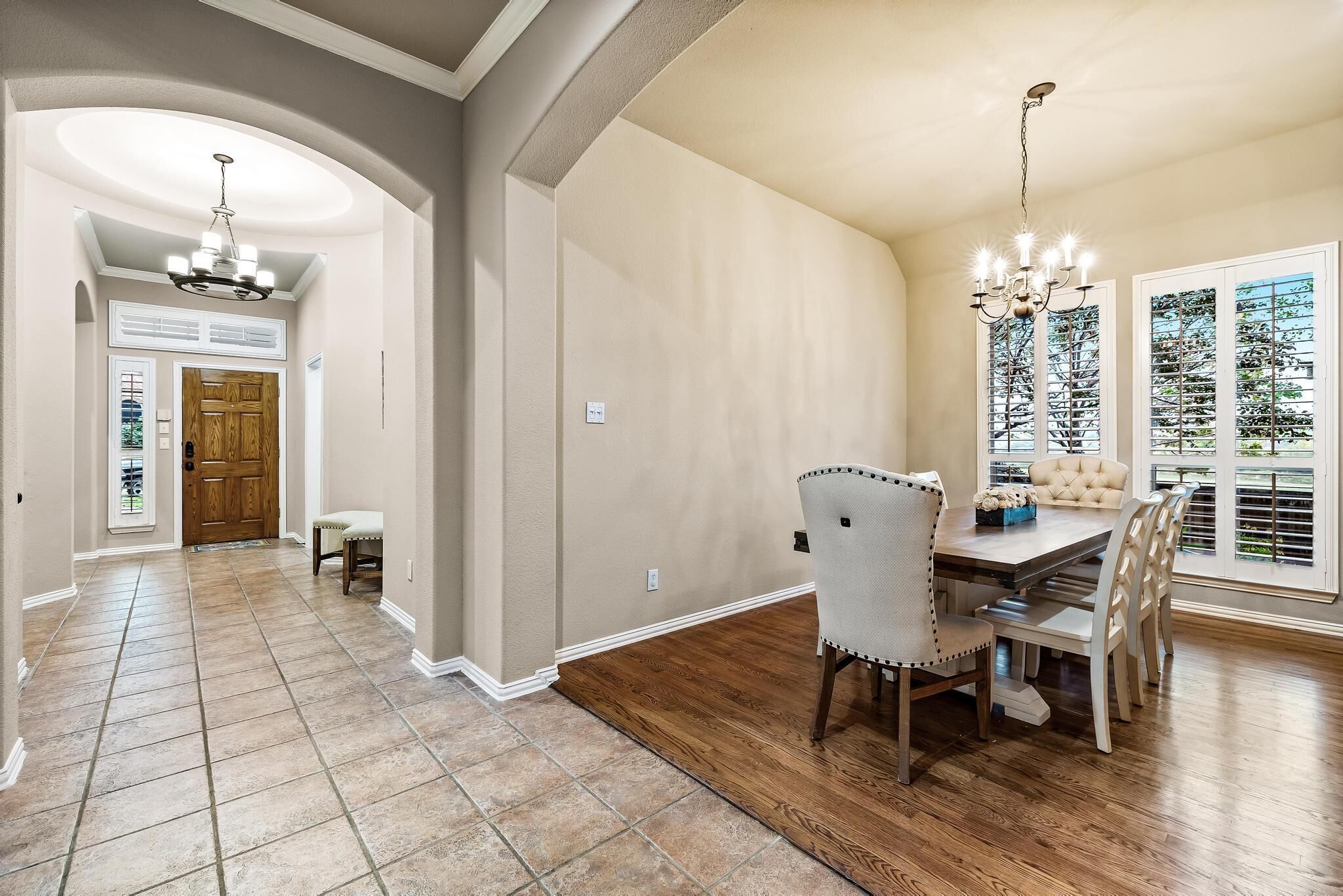 A spacious dining area with a wooden table and chairs, a chandelier, and a view of trees through the windows.