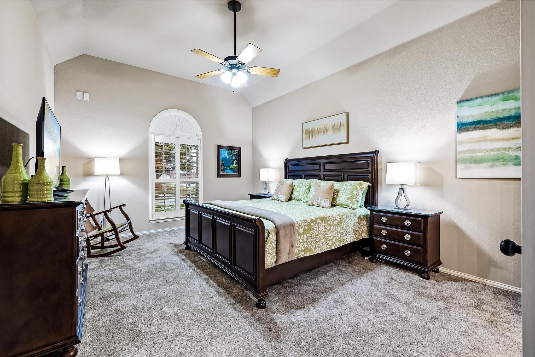 A bedroom with a bed, dresser, nightstands, and a ceiling fan.
