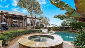 Un patio trasero con un jacuzzi de piedra, zona de barbacoa y piscina.