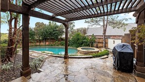 Un patio cubierto con suelo de piedra, piscina y jacuzzi.