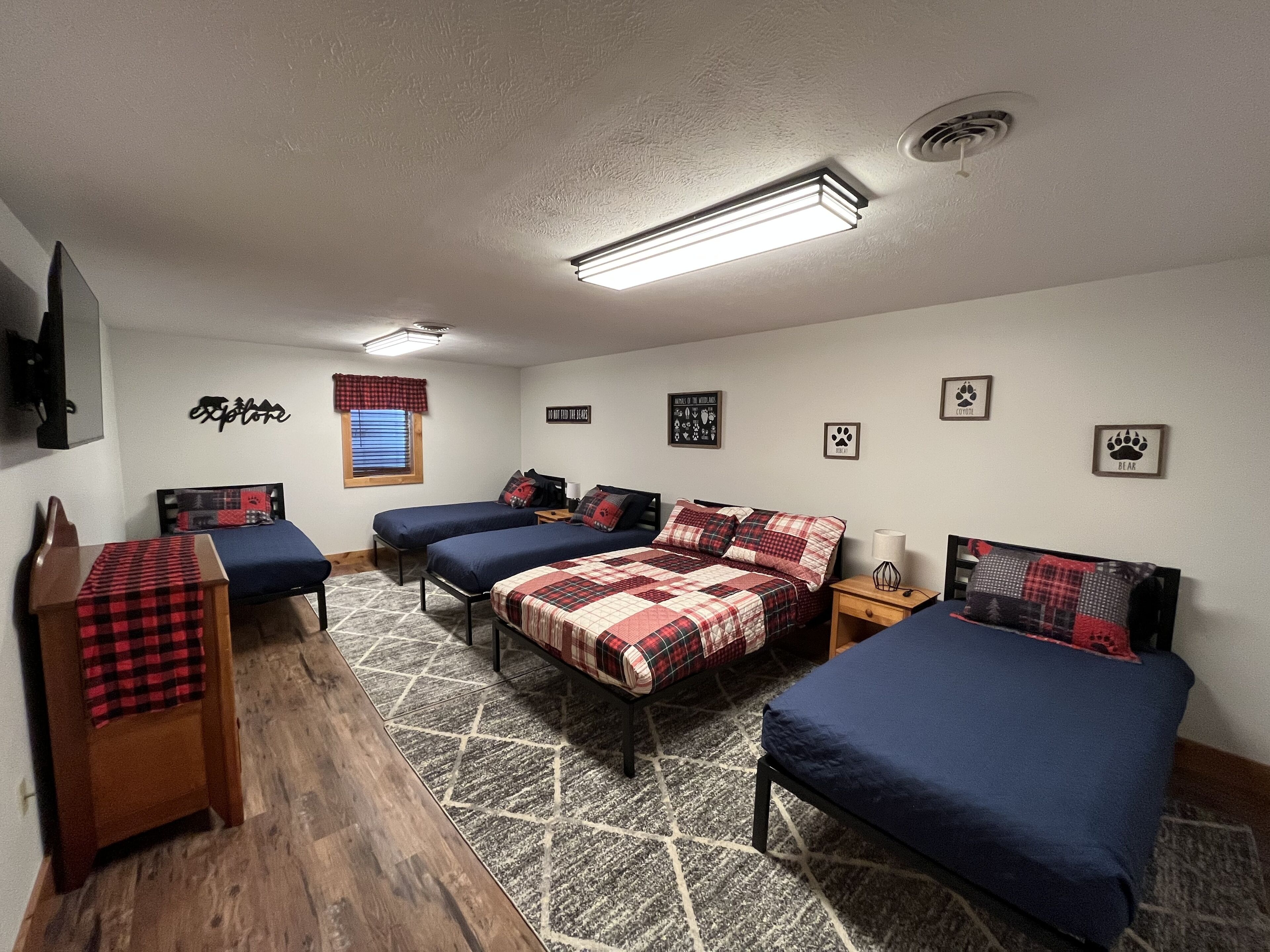 A room with two single beds, a desk, a chair, a window with blinds, and a ceiling light fixture.
