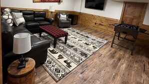 Un salon avec un canapé en cuir noir, un tapis à motifs, une table basse en bois, une lampe et une table de baby-foot.