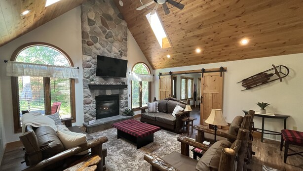 Un salon chaleureux avec une cheminée en pierre, un plafond en bois et de grandes fenêtres.