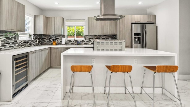 Una cocina moderna con una isla central, taburetes de bar y un refrigerador de acero inoxidable.