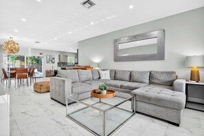 Un salon moderne avec un canapé d’angle, une table basse en verre et un coin repas comprenant une table et des chaises.
