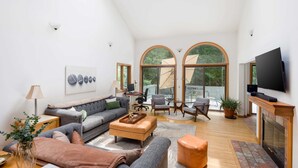 Un salon spacieux avec un haut plafond, une cheminée, un téléviseur et un balcon doté de grandes fenêtres.
