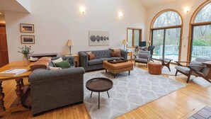 Un salon spacieux avec un canapé gris, une table basse en bois et une grande fenêtre donnant sur les arbres.