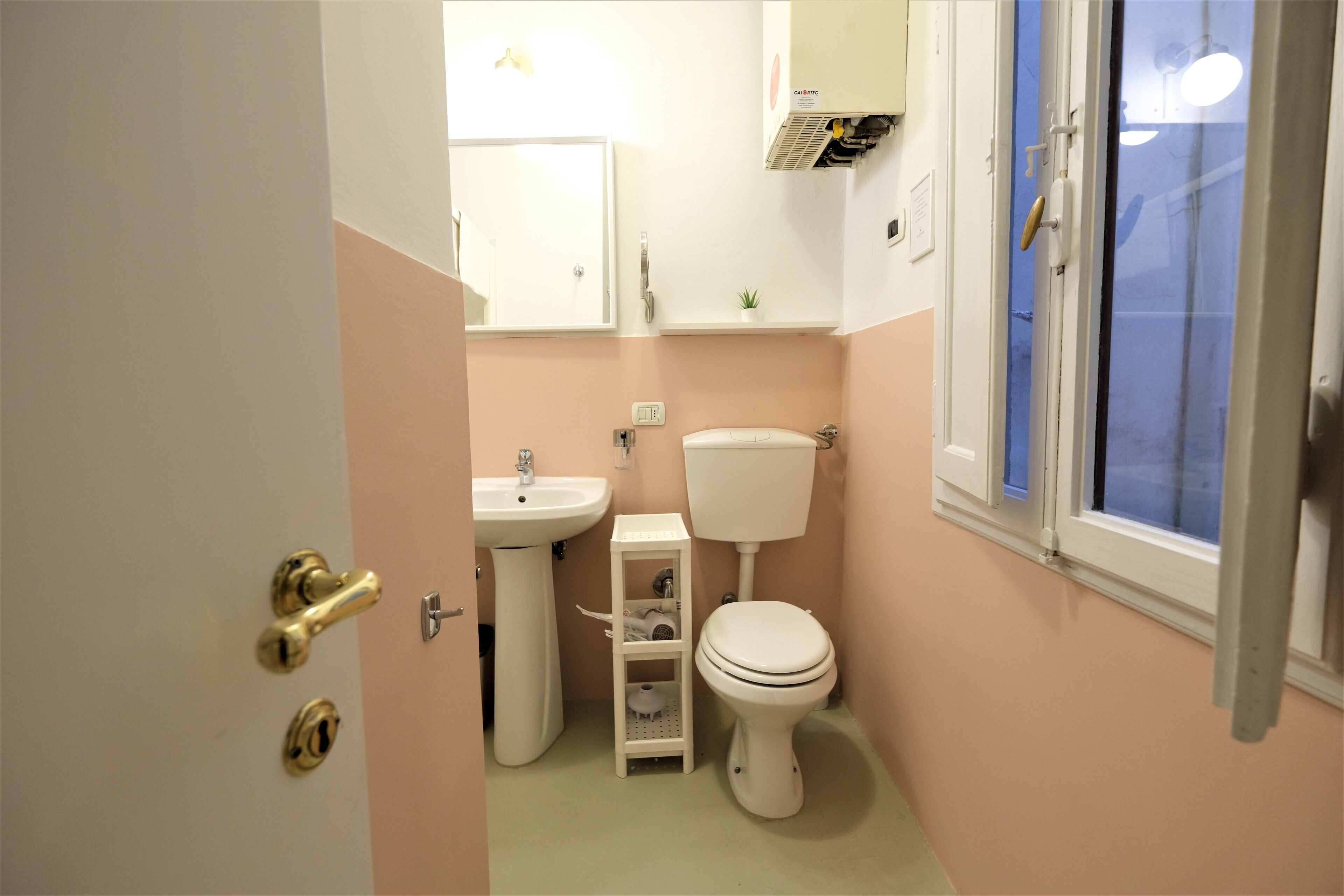 A bathroom with a toilet, sink, and a small shelf unit.