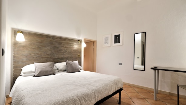 A bedroom with a bed, bedside lamps, a nightstand, a mirror, and two framed pictures on the wall. - Wine Apartments Florence Dolcetto (Florence)
