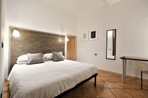 A bedroom with a bed, bedside lamps, a nightstand, a mirror, and two framed pictures on the wall. - Wine Apartments Florence Dolcetto (Florence)