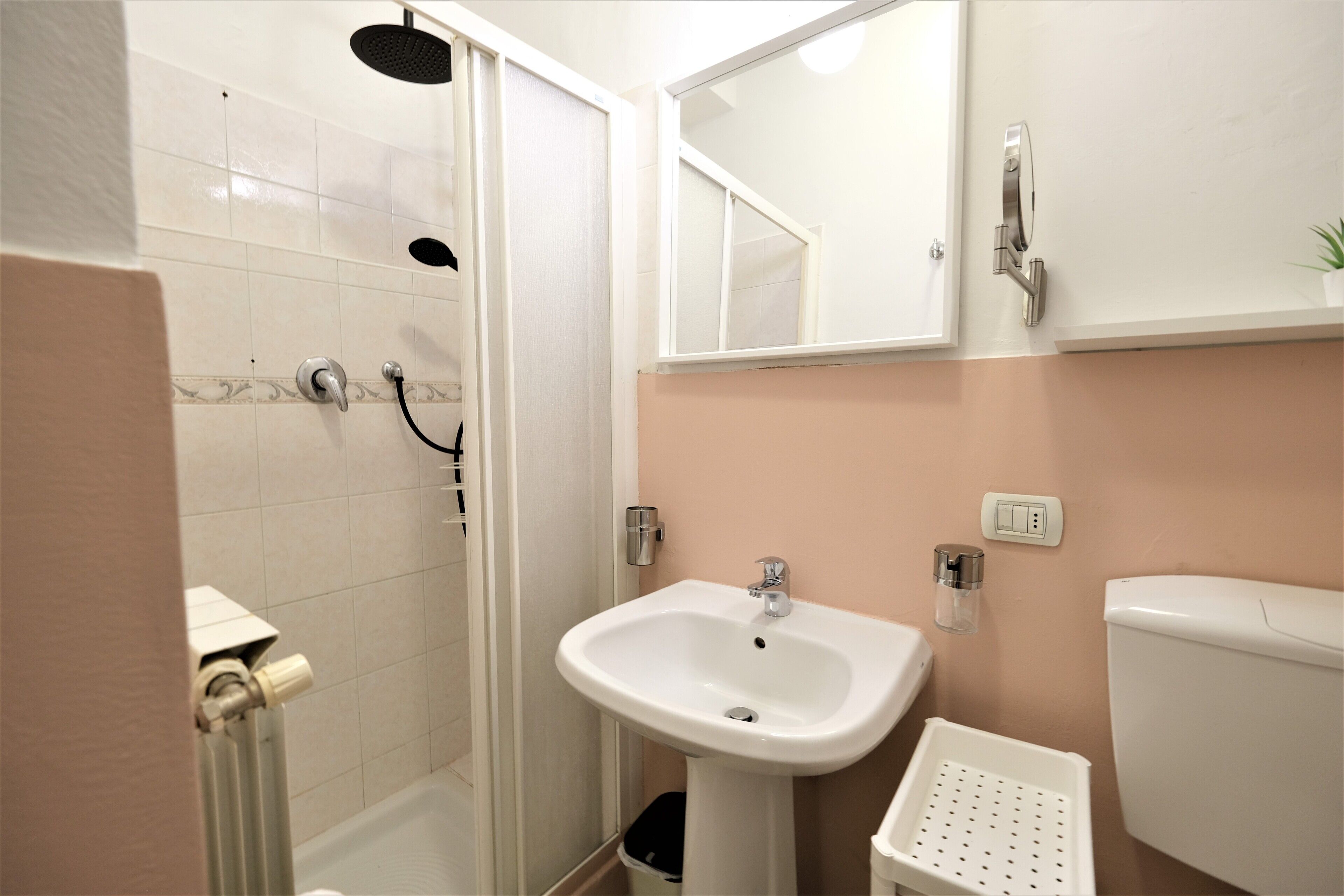 A bathroom with a shower, sink, toilet, and a small trash bin.
