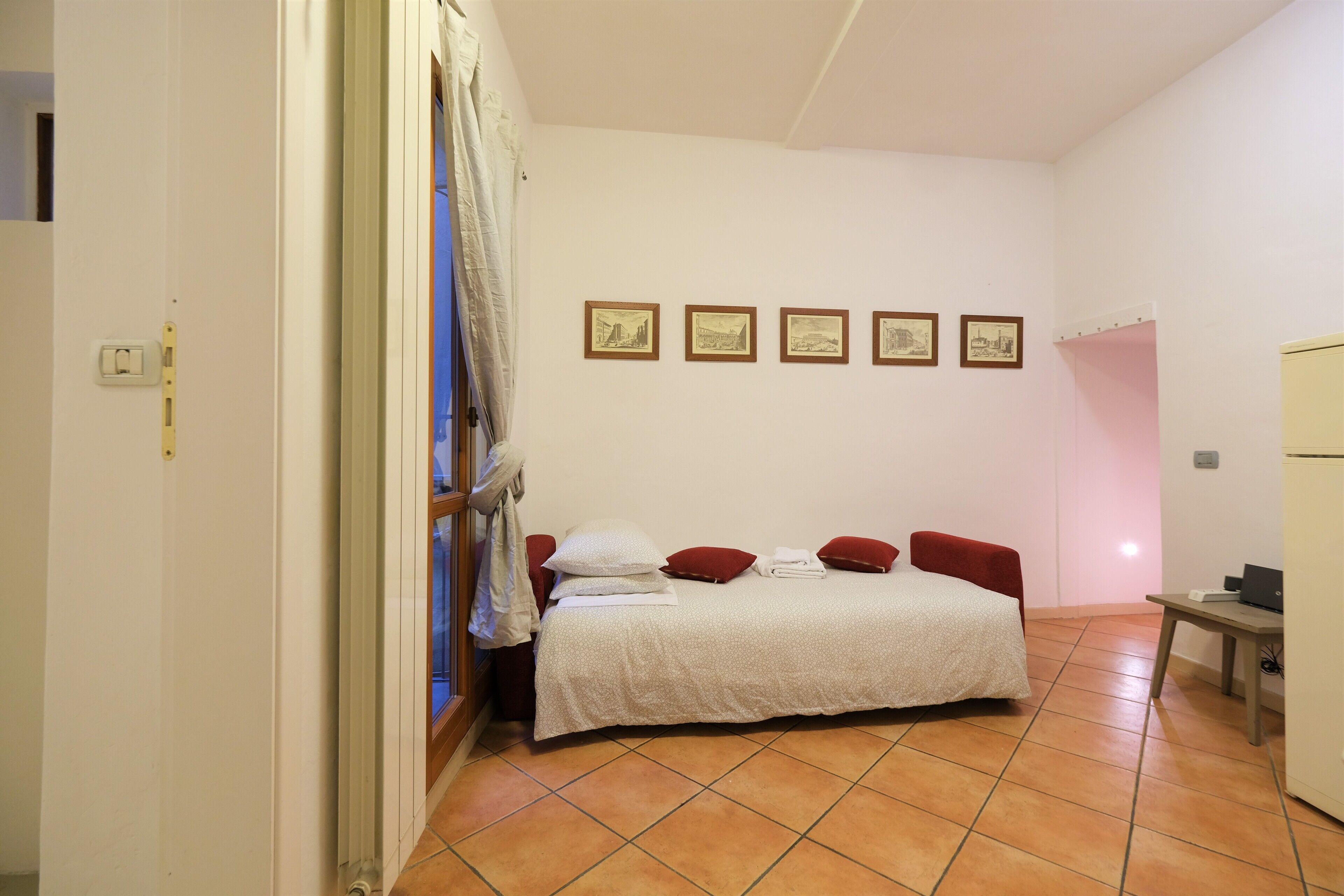 A bedroom with a bed, a desk, and a chair. There are five framed pictures on the wall.