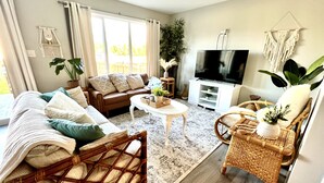 A living room with a sofa, coffee table, TV, and wicker chairs. - Gorgeous townhome 5 min walk to the stunning lake. (Sylvan Lake)
