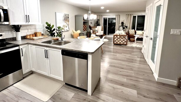 A modern kitchen with white cabinets, a dishwasher, and a dining area with a wooden table and chairs. - Gorgeous townhome 5 min walk to the stunning lake. (Sylvan Lake)