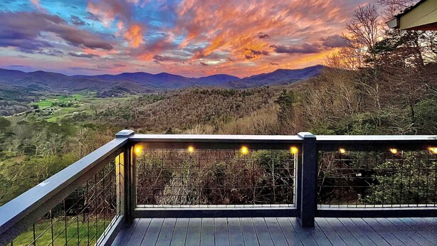 A deck with a railing overlooking a valley with distant mountains and a colorful sky. - Almost Heaven - Mountain views beyond compare! (Hiawassee)
