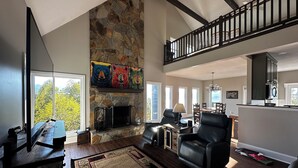 A spacious living room with a stone fireplace, a dining area, and a kitchen. - Almost Heaven - Mountain views beyond compare! (Hiawassee)