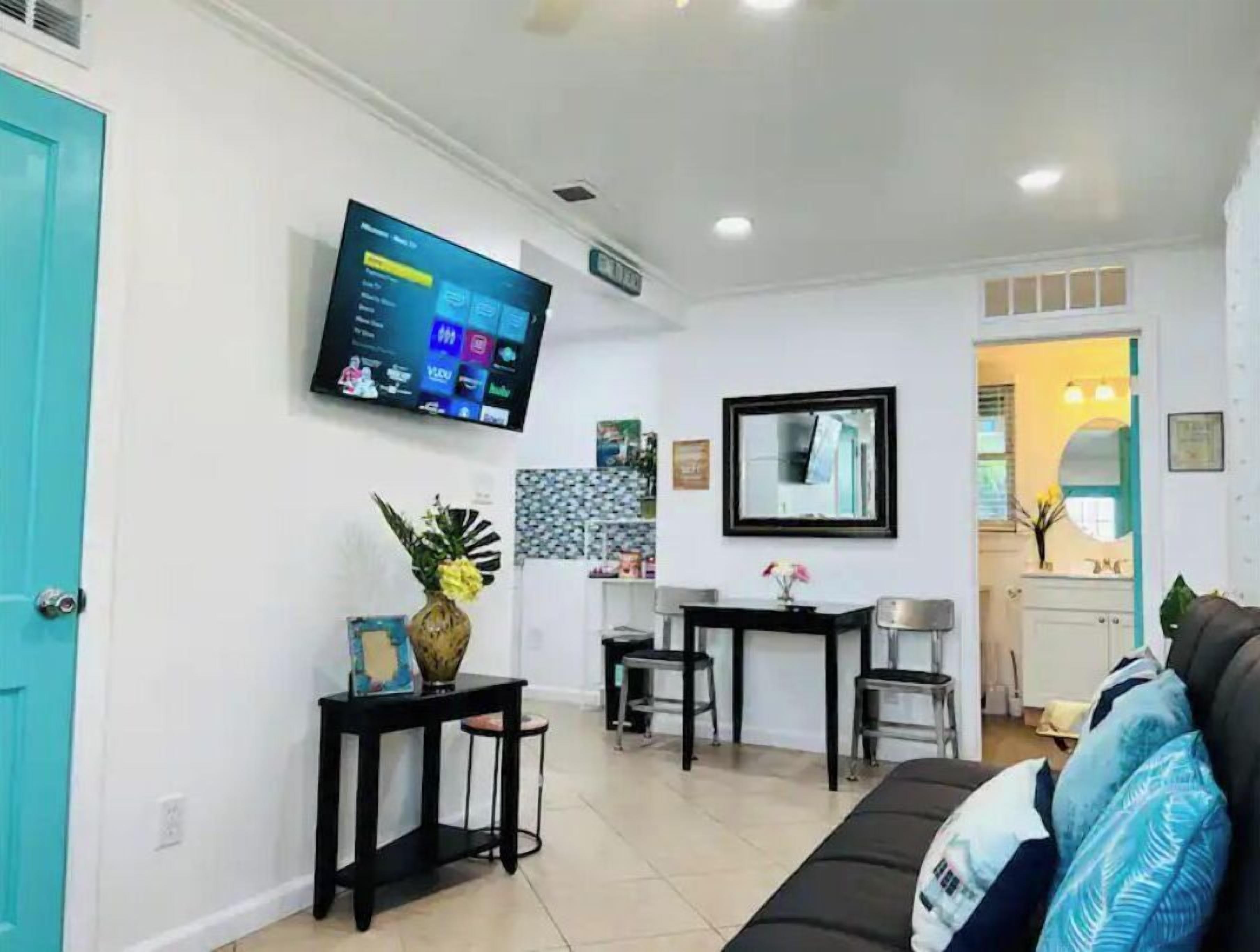 Ein Wohnzimmer mit Fernseher, einem Konsolentisch mit Vase, einer Couch mit Kissen und einem Essbereich mit Stühlen.