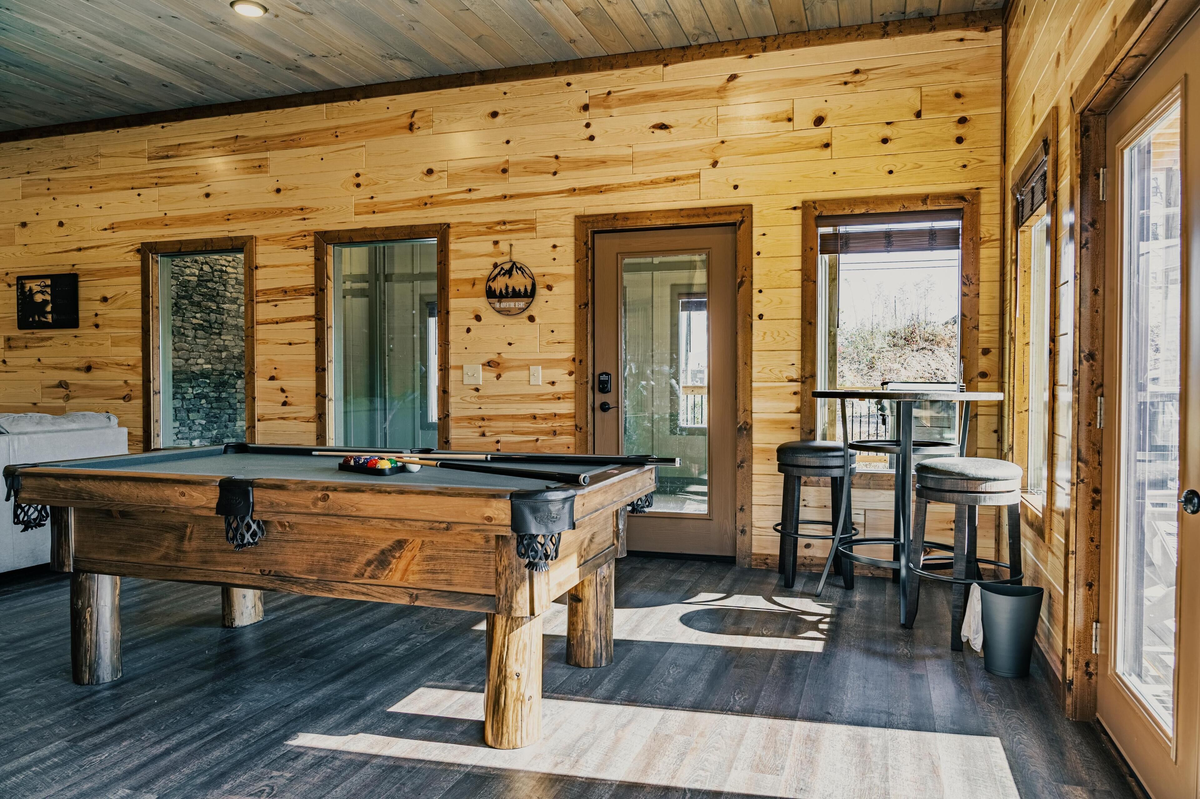 Een houten interieur met een pooltafel, barstoelen en een accentmuur van steen.