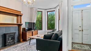 Ein modernes Wohnzimmer mit Kamin, Fernseher, einer Couch und einem großen Fenster mit Blick auf Bäume.