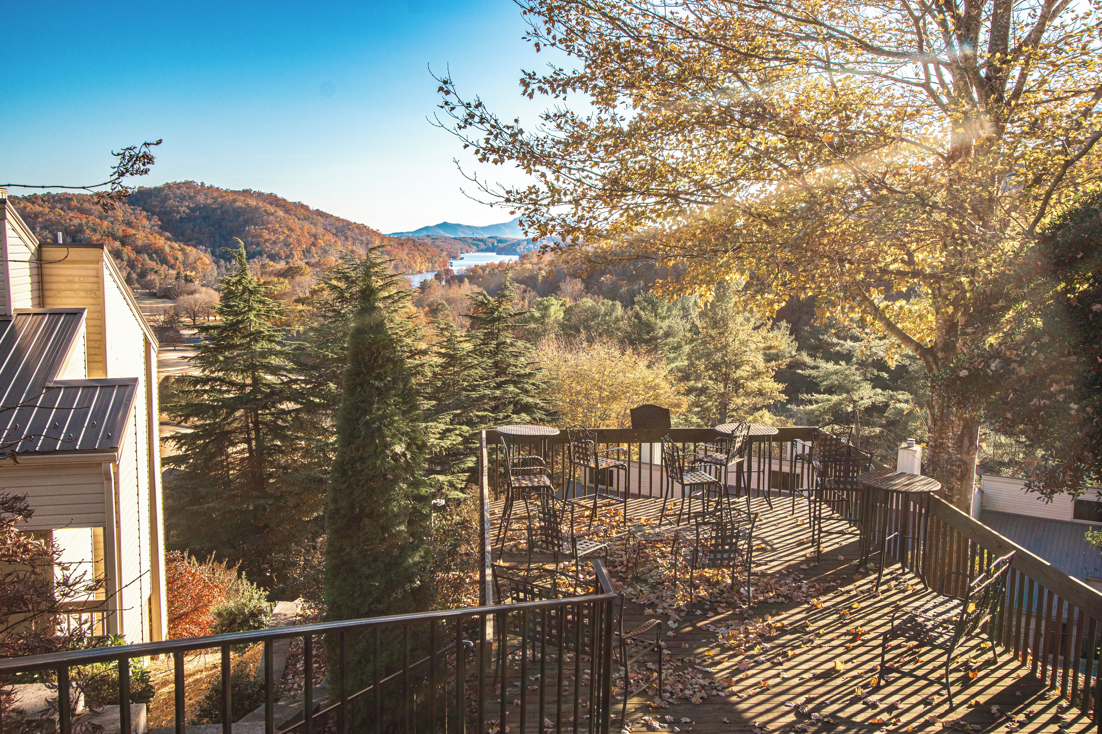 A wooden deck with chairs and a table, surrounded by trees and a mountain view.