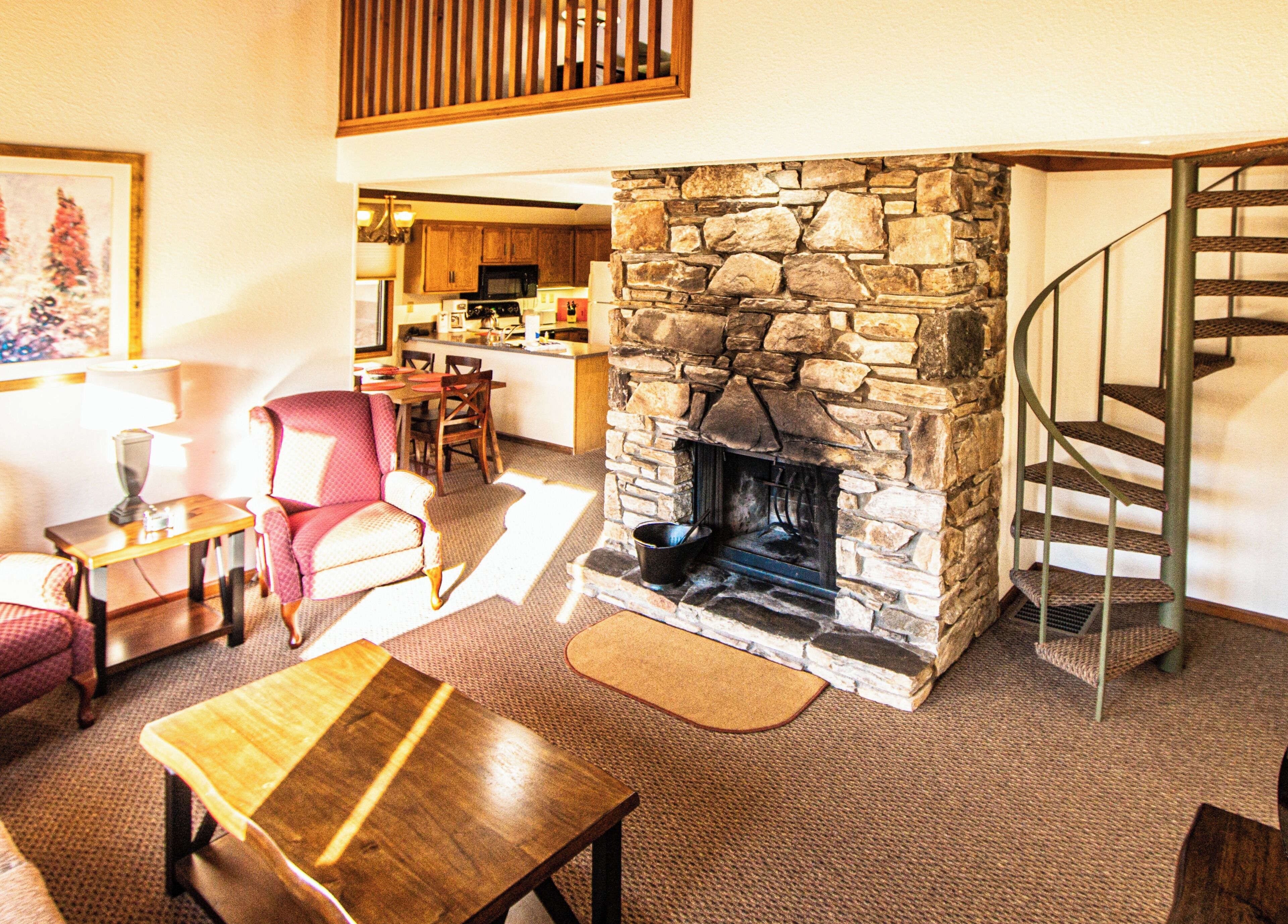 A living room with a stone fireplace, a dining area, and a kitchen in the background.