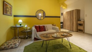 Ein Wohnzimmer mit gelber Wand, einem runden Spiegel, einem Sofa, einem Couchtisch und einem grünen Teppich.