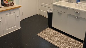 A compact kitchen with white cabinets, a black countertop, a sink, and a patterned rug.