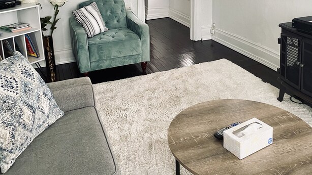 A living room with a green armchair, a gray sofa, a coffee table, and a TV on the wall.