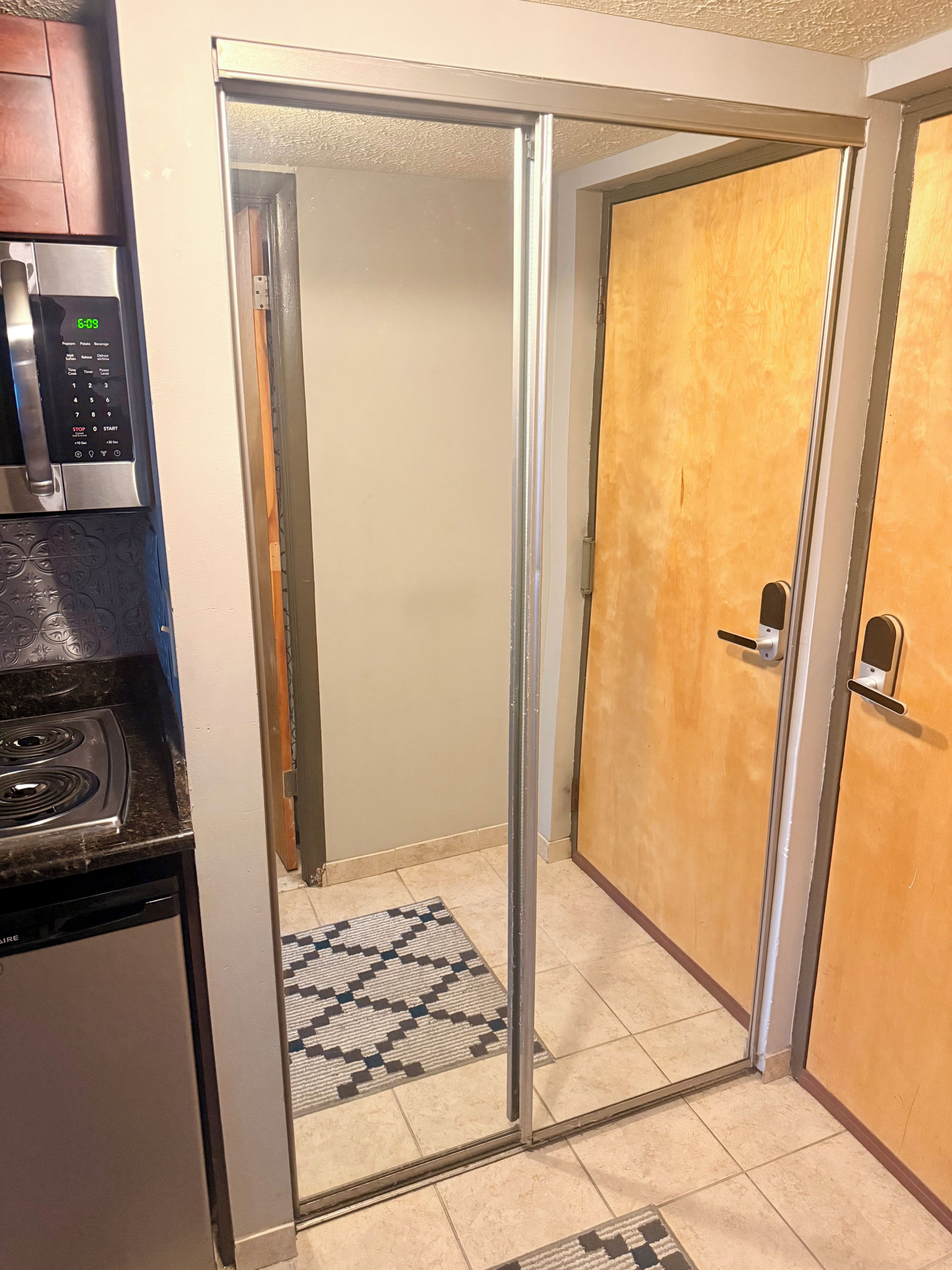 Una cucina con forno a microonde, piano cottura e lavastoviglie. Una porta scorrevole in vetro dà accesso a un corridoio con tappeto decorato.