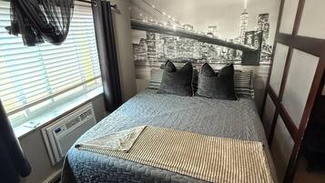 A bedroom with a cityscape mural, a bed with striped bedding, a chandelier, and a window with curtains.
