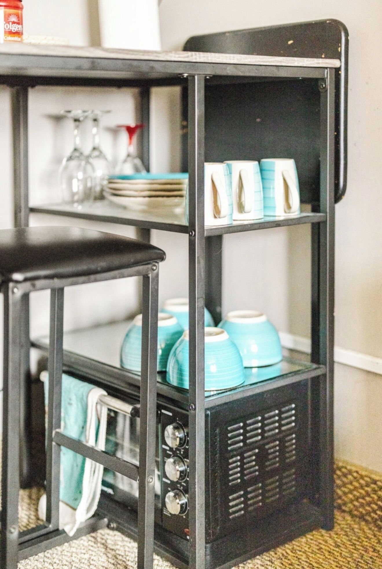 A kitchen area with a black metal shelf unit holding dishes and blue ceramic pots.